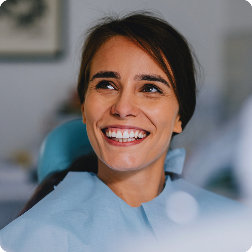 Smiling female patient sitting in a dental chair during a dental appointment, showing confidence and satisfaction with her oral health care.